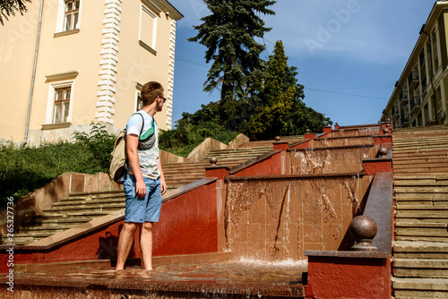 happy stylish hipster man playing with water in fountain, having fun, summer vacation
