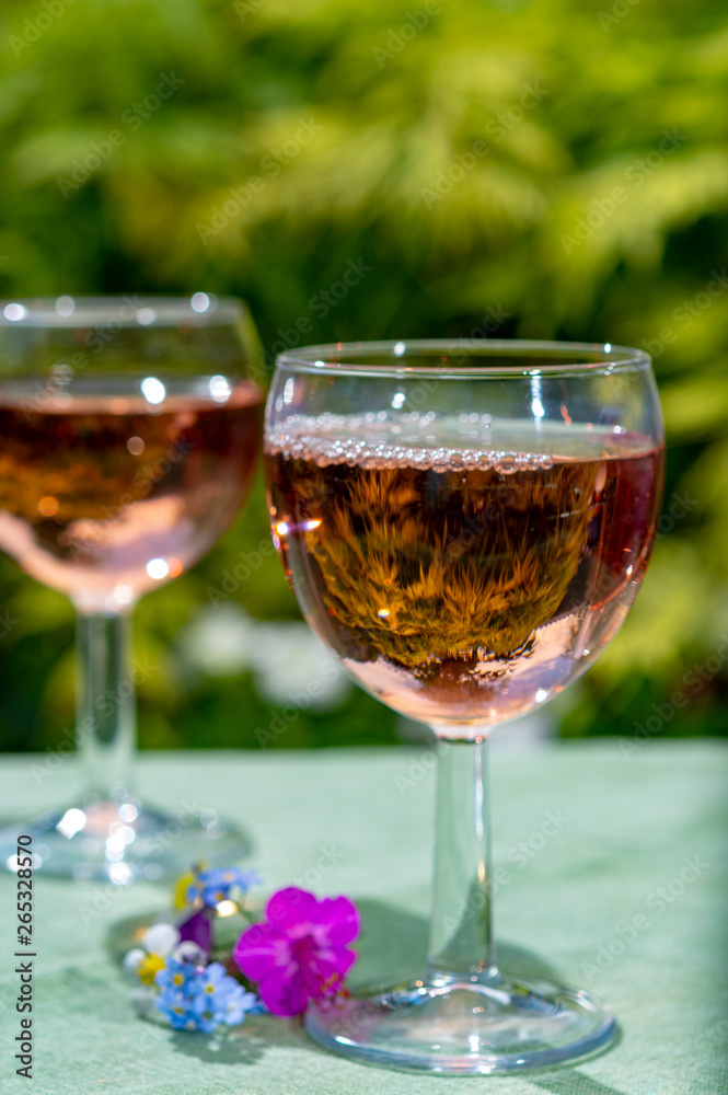 Waiter pouring cold rose wine in glasses in summer sunny day in blossoming garden Waiter pouring cold rose wine in glasses in summer sunny day in blossoming garden