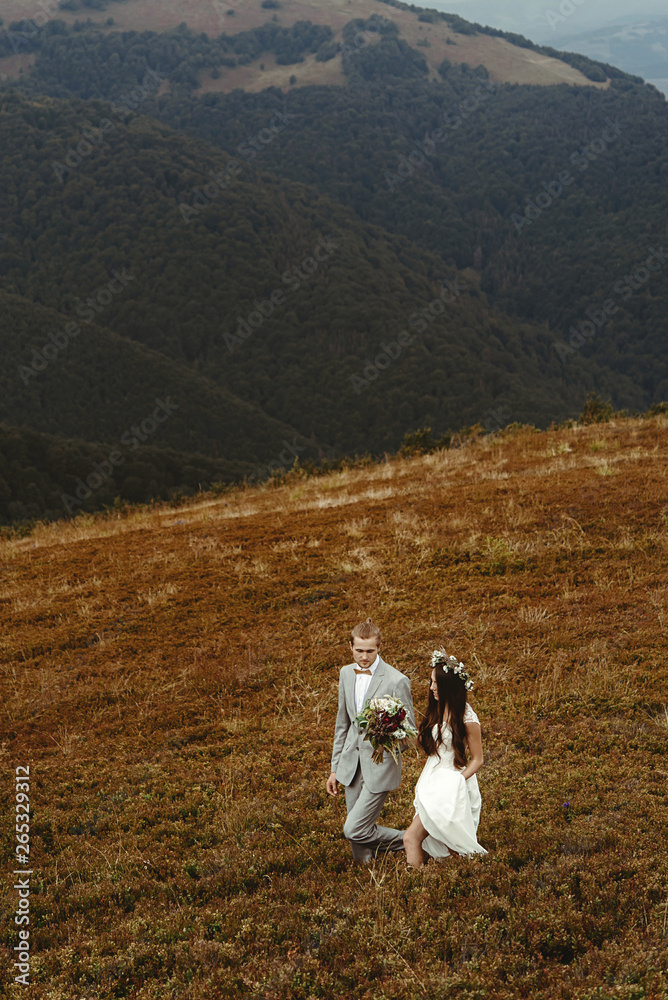 gorgeous bride and stylish groom walking,  boho wedding couple, luxury ceremony at mountains with amazing view, space for text