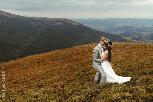 gorgeous bride and stylish groom hugging, boho wedding couple, luxury ceremony at mountains with amazing view, space for text