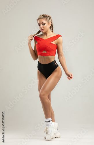 Happy young woman in sports clothing. Muscular fitness model on grey background. Red and black clothes.
