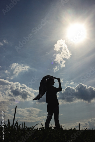 Fototapeta Naklejka Na Ścianę i Meble -  silhouette of stylish girl holding scarf in the windy evening outdoors in spring field, life success happiness concept