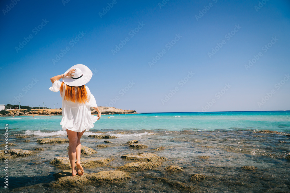 Woman tourist white dress standing on beach with crystal clear water.