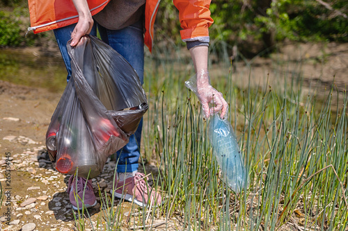 Volunteer collects plastic blue bottle near the river. The concept of environmental protection photo