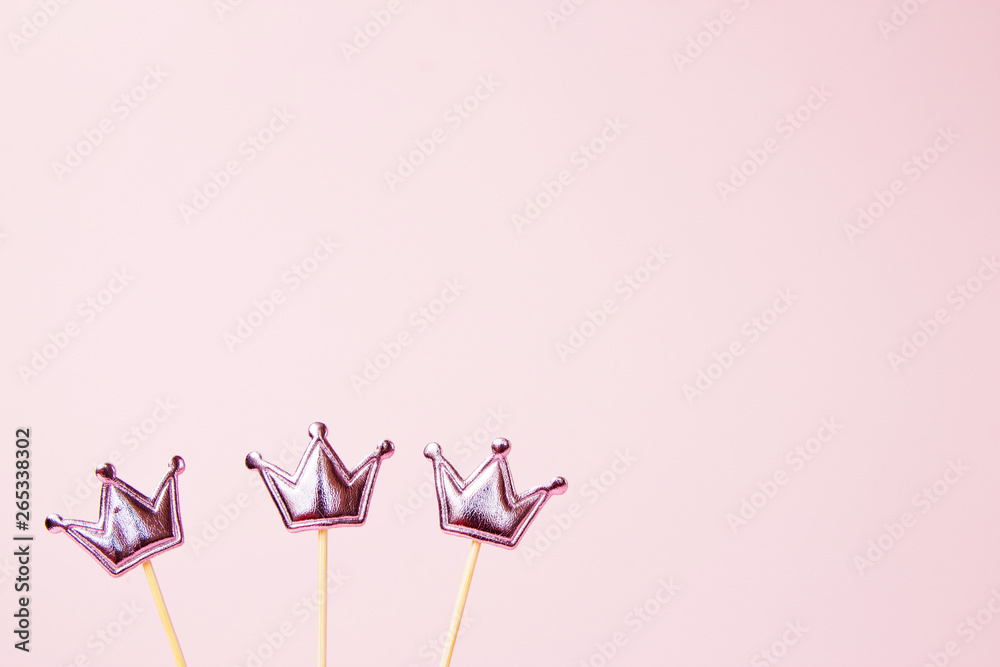 Three shiny crowns on a pink background. Decorations for holiday party. Copy space