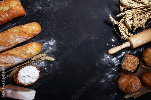 Assortment of baked bread and bread rolls on rustic black bakery table background