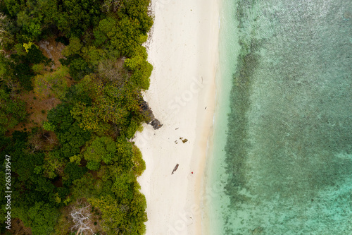 Aerial drone view of a deserted, idyllic tropical sandy beach on a small, lush green island