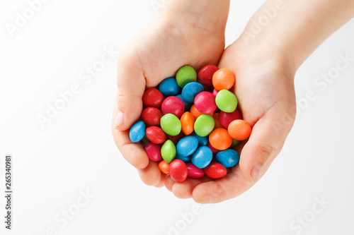 Multicolored candies in the hands of a child on a white isolated background