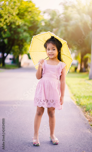 little girl in pink dress with yellow umbrella in sunny day