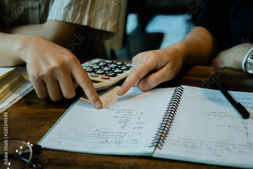 Asian young man and woman sitting pointing studying examining and using calculator tutor Math books with friends, Young students campus helps friend catching up as learning. People learning education