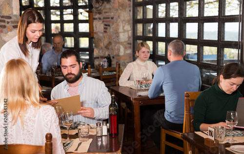 Charming young waiter receiving order from guests in country restaurant