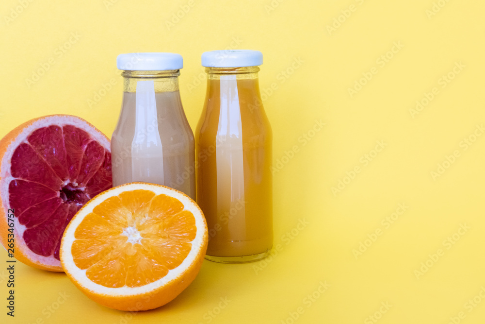 Raw fruit juices in glass bottles on yellow background. Copy space Raw fruit juices in glass bottles on yellow background. Copy space