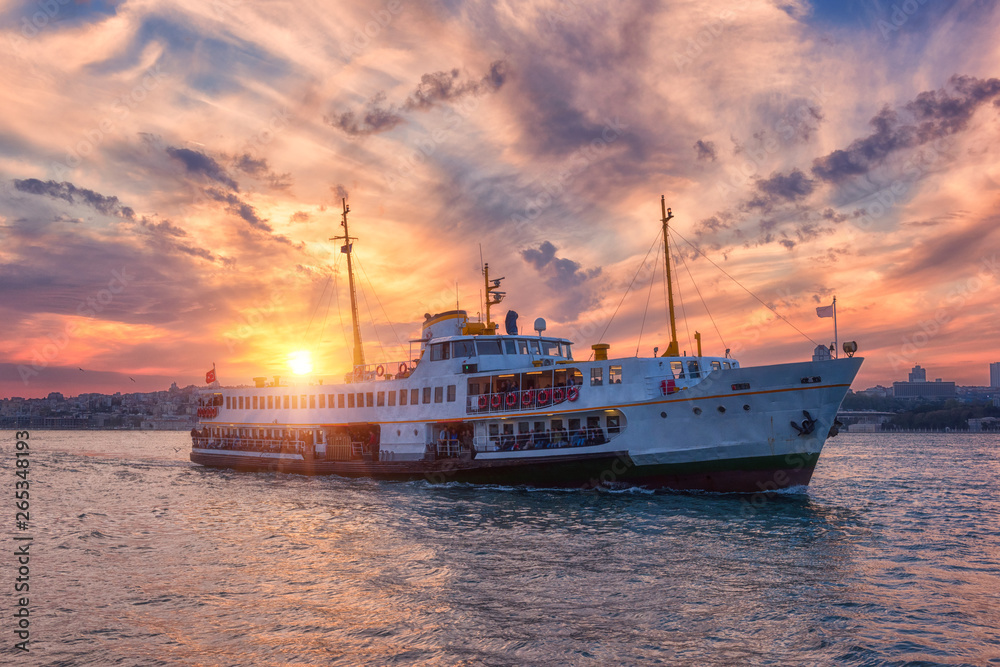 Amazing color sunset over Bosphorus with passenger boat (river tram) and sun, Istanbul, Turkey. Scenic travel background
