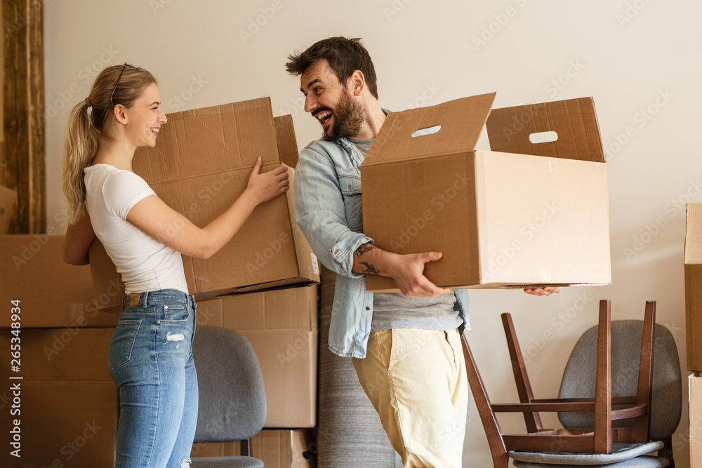 Young couple carrying big cardboard box into new home.Moving house. - obrazy, fototapety, plakaty 