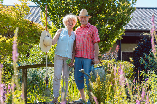 Portrait of an active senior couple holding gardening tools in the garden