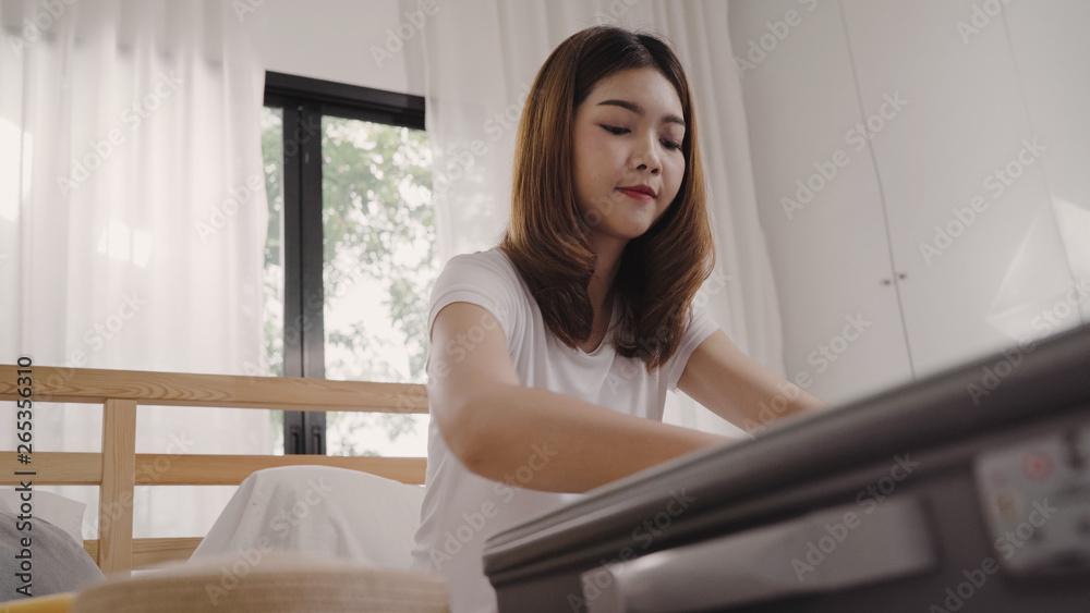 Beautiful young Asian woman traveler packing stuff in suitcase prepare for holiday vacation while lying on the bed when relax in her bedroom at home. Lifestyle women backpacker travel concept.