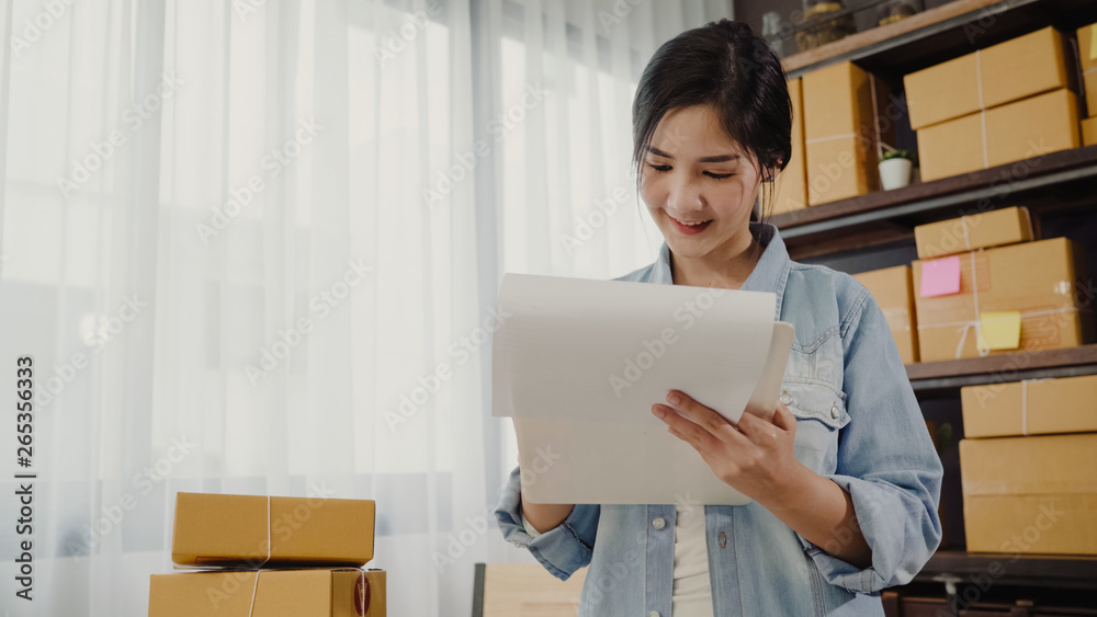 Beautiful smart Asian young entrepreneur business woman owner of SME checking product on stock and write on clipboard working at home. Small business owner at home office concept. Beautiful smart Asian young entrepreneur business woman owner of SME checking product on stock and write on clipboard working at home. Small business owner at home office concept.