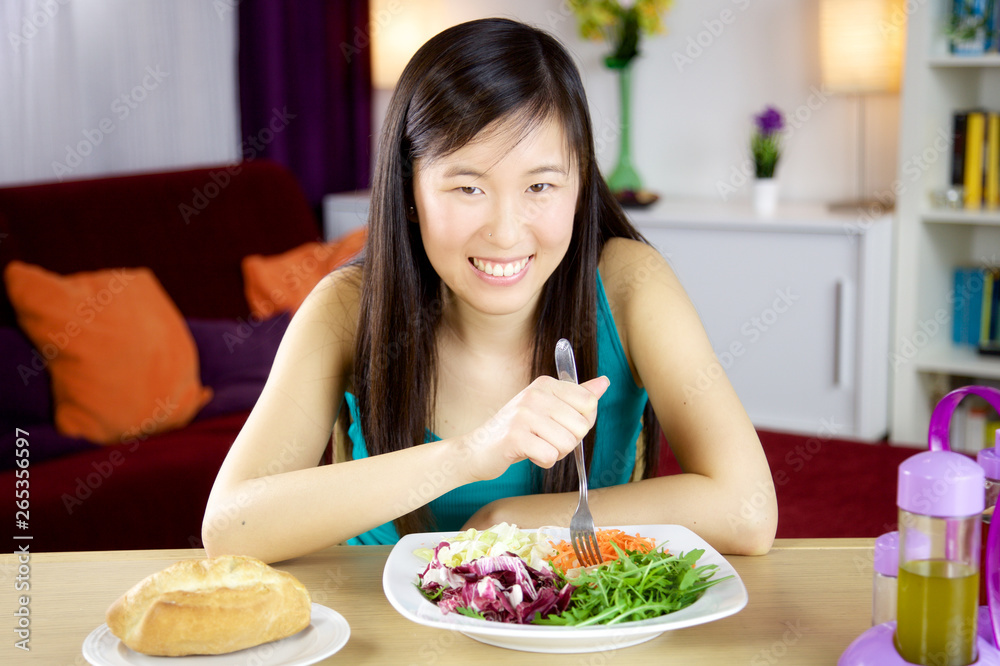 Happy asian woman eating salad at home smiling medium shot Happy asian woman eating salad at home smiling medium shot