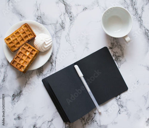 notebook with black sheets on marble background and waffles photo