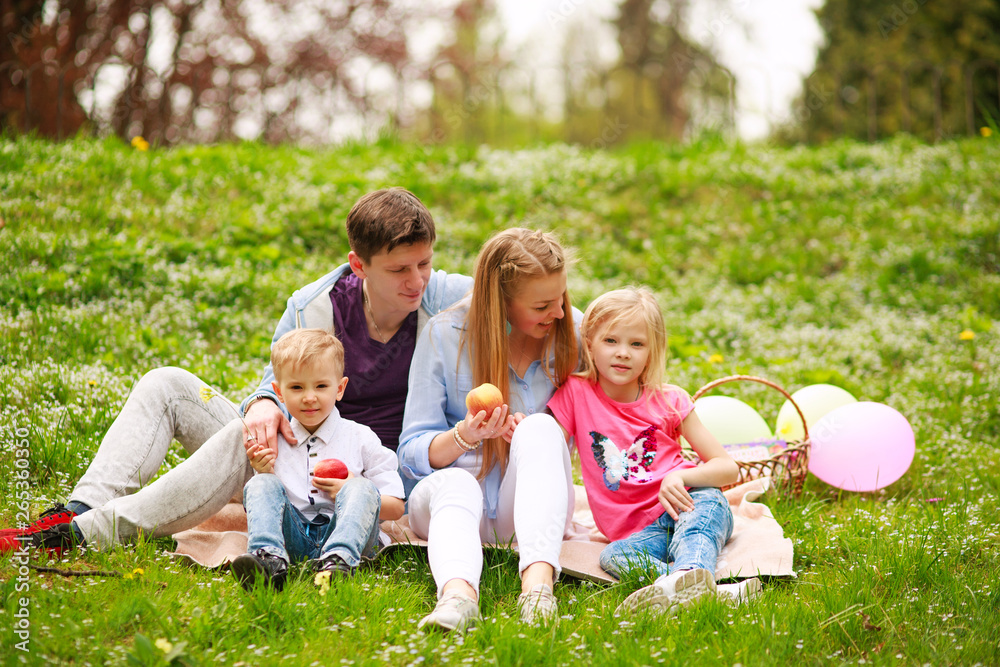 Happy family on picnic in flowered park sitting on grass, parenthood leisure in nature Happy family on picnic in flowered park sitting on grass, parenthood leisure in nature