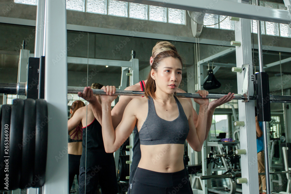 Sporty girl doing weight exercises with assistance of her personal trainer.sport, fitness, teamwork, bodybuilding and people concept Sporty girl doing weight exercises with assistance of her personal trainer.sport, fitness, teamwork, bodybuilding and people concept