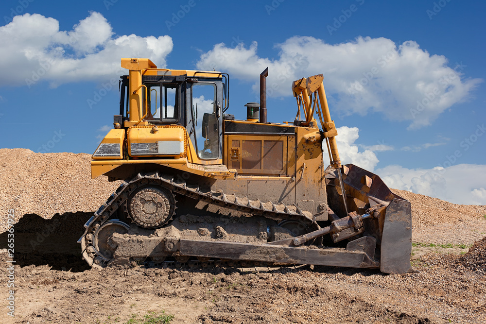 Yellow dozer on a dirt terrain with blue sky with clouds in the background Yellow dozer on a dirt terrain with blue sky with clouds in the background