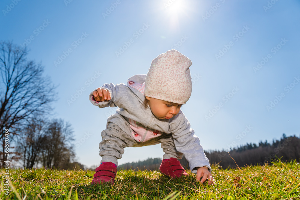 Baby wearing warm beanie hat, sweatshirt and red boots outdoors in rural area discovering nature in spring, sunny day. Baby wearing warm beanie hat, sweatshirt and red boots outdoors in rural area discovering nature in spring, sunny day.