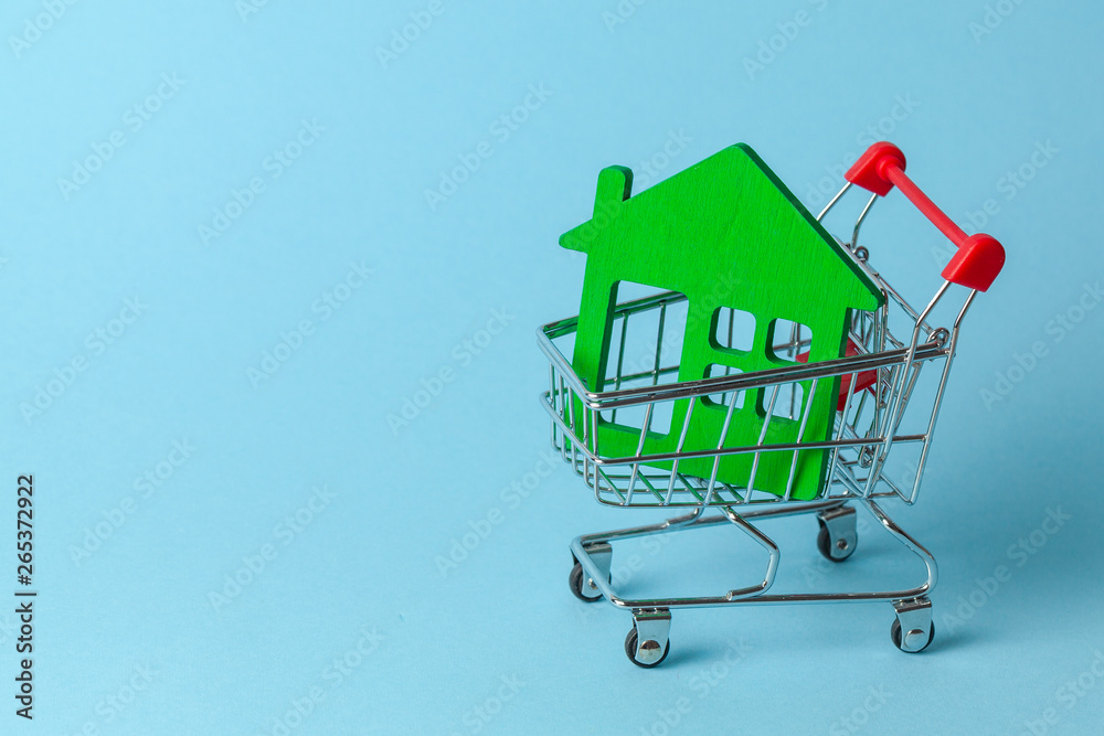 Shopping cart and house on a blue background. Buying and selling real estate. Copy space for text. Shopping cart and house on a blue background. Buying and selling real estate. Copy space for text.