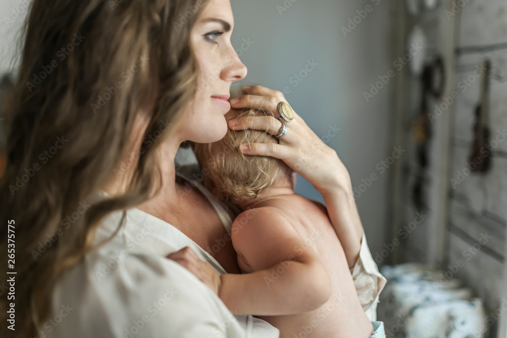 A mother holds her young baby girl and cradles her head with her hand while snuggling after nap time; Sorrento, British Columbia, Canada