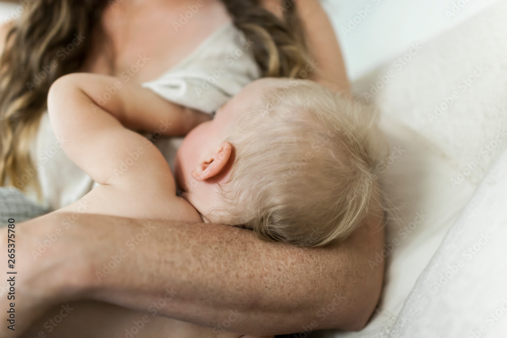 A mother holds her young baby girl and  breastfeeds her on her bed; Sorrento, British Columbia, Canada