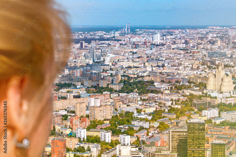 The girl looks at the Sunny city. A woman sees the house and down the road. The view from the observation deck of Moscow