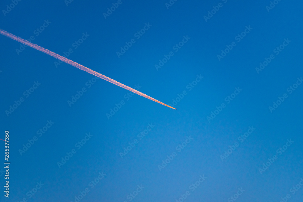 Orange contrails of an airplane at sunset and bright blue sky. Scene reminiscent of technology, transport, nature and holidays at the same time Orange contrails of an airplane at sunset and bright blue sky. Scene reminiscent of technology, transport, nature and holidays at the same time