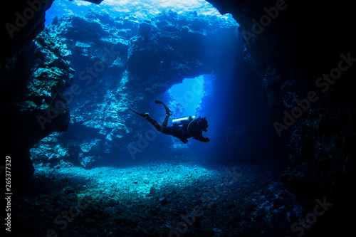 Scuba diver swims through lava arches with sun rays, Cathedrals dive site; Lanai City, Lanai, Hawaii, United States of America