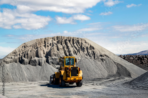 A large wheel loader heavy equipment machine is parked in front of a gravel pile in the mountain landscape; Iceland photo