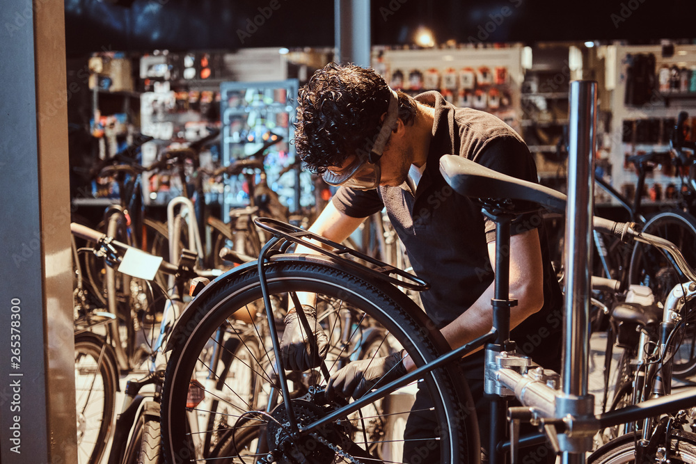 Obraz premium Pensive diligent master in protective glasses is fixing bicycle at workshop.