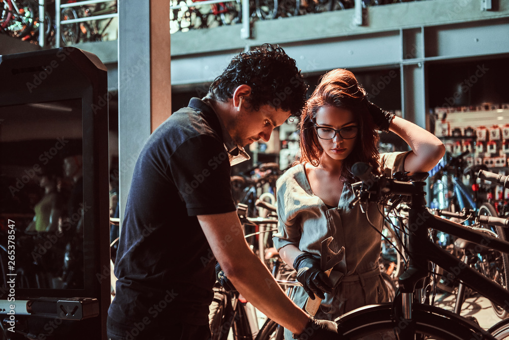 Young master and his attractive apprentice are fixing customer's bicycle at workshop.