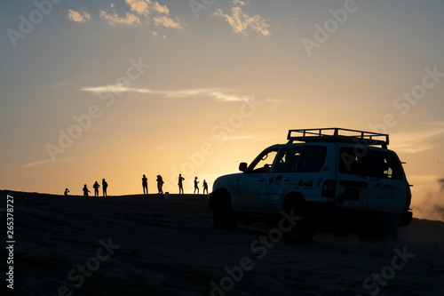 4x4 car on top of sand dune at sunset with people watching the setting sun © Yassine