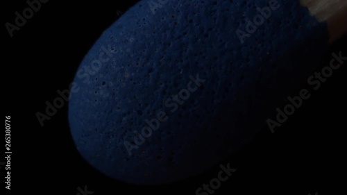 Extreme macro of blue matchstick igniting, burning and fuming in slowmotion on black background