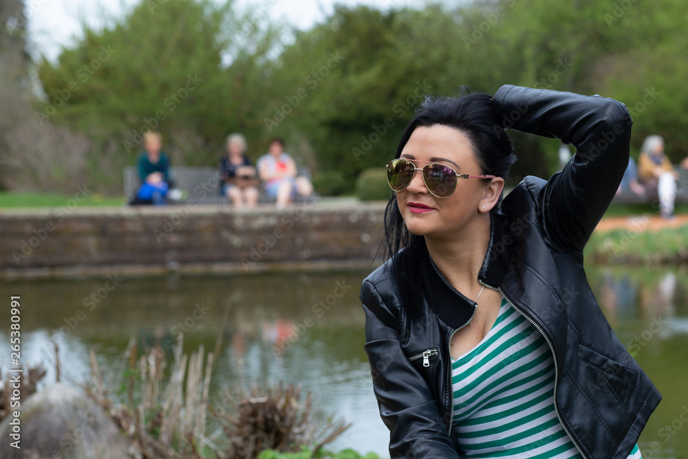 Brunette in sunglasses and a black jacket sits and enjoys the sun in the park Brunette in sunglasses and a black jacket sits and enjoys the sun in the park