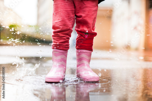 Child standing with pink rubber boots in puddle in rain. Kind steht mit rosa Gummistiefeln in Wasserpfütze im Regen.
