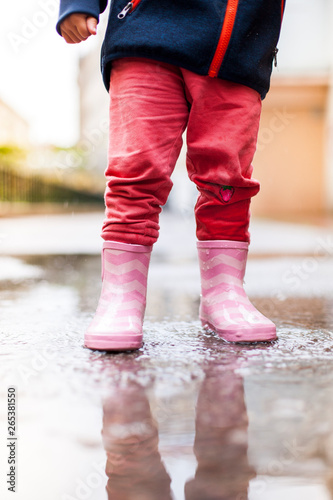 Child standing with pink rubber boots in puddle. Kind steht mit rosa Gummistiefeln in Wasserpfütze.