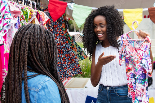 Beautiful african american market vendor presenting clothes to customer photo