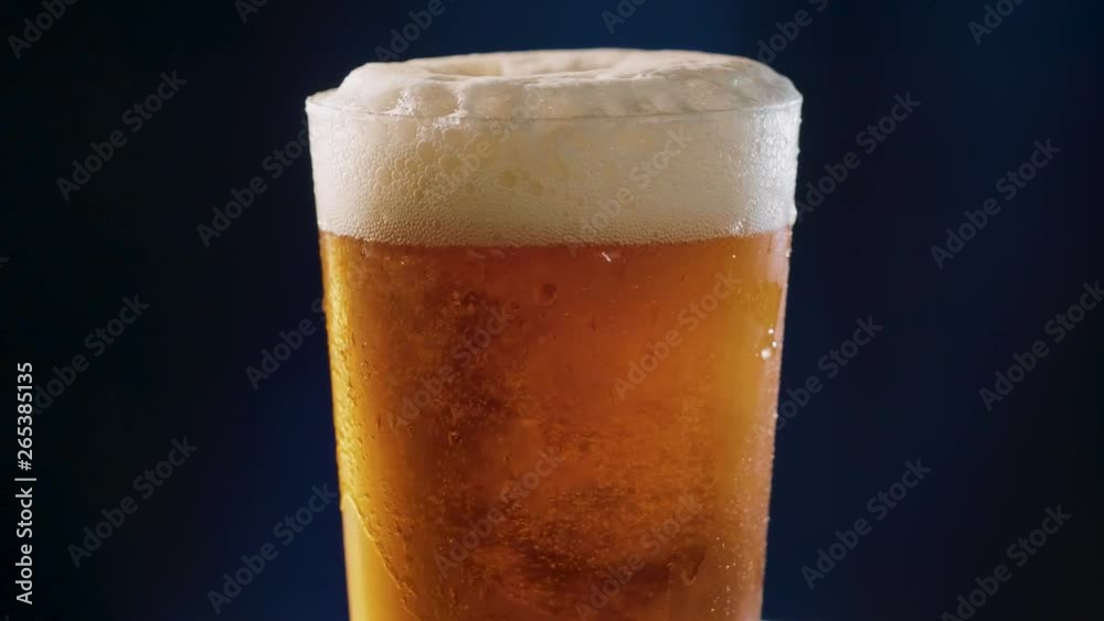 Golden Beer poured to a glass, rotating over a dark blue background, slow motion. Golden Beer poured to a glass, rotating over a dark blue background, slow motion.