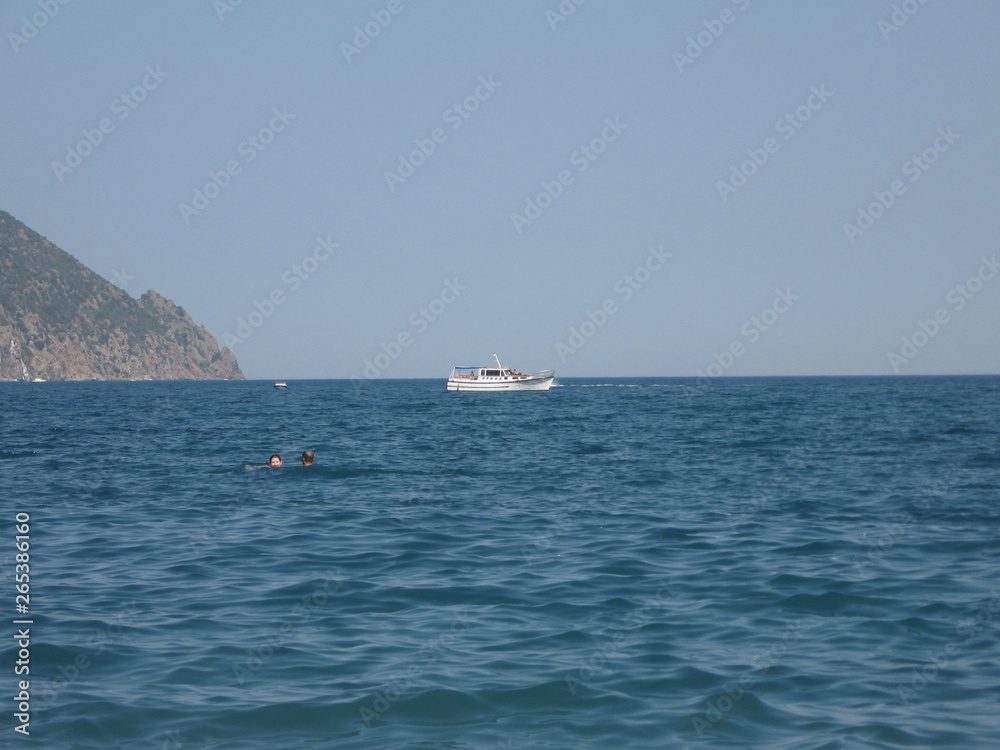 a white yacht is sailing in the sea not far from the mountain on a sunny day