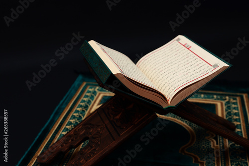 Islamic Holy Book Quran on wood carving rahle with rosary beads and prayer rug on black background. Kuran the holy book of Muslims. Ramadan concept.
