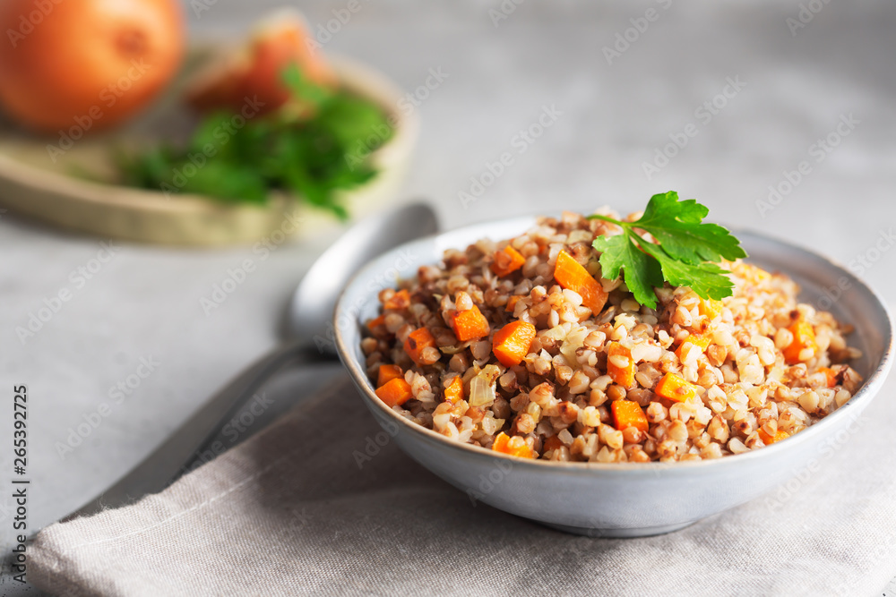 Boiled buckwheat cereal with carrot, parsley and butter in a bowl on a dark background. Traditional Russian dish on gray background Boiled buckwheat cereal with carrot, parsley and butter in a bowl on a dark background. Traditional Russian dish on gray background