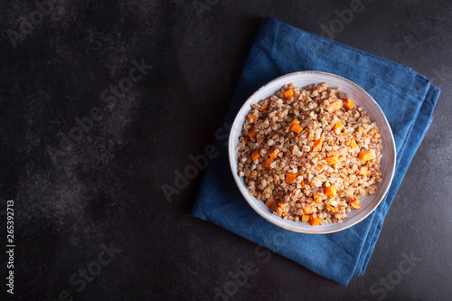 Boiled buckwheat cereal with carrot, parsley and butter in a bowl on a dark background. Traditional Russian dish on dark background with copy space