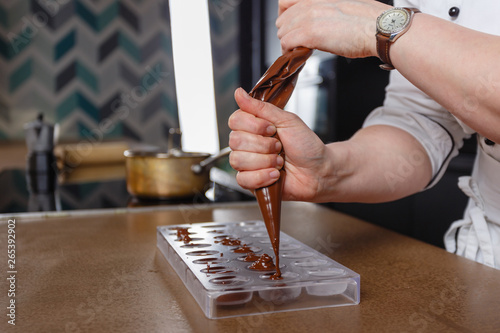 Wallpaper Mural Chocolatier pours chocolate into molds. Chef in white apron using pastry bag filling hot melt chocolate into silicone mold. Concept for making homemade chocolate dessert in modern clean kitchen. Torontodigital.ca