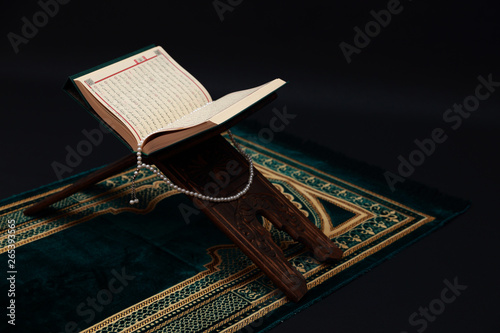 Islamic Holy Book Quran on wood carving rahle with rosary beads and prayer rug on black background. Kuran the holy book of Muslims. Ramadan concept. photo