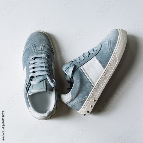 A pair of blue suede sneakers on a white sole with white accents on a white background